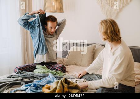 Young gay couple talking and smiling while sitting in bed at home Stock Photo