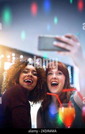 Its the weekend yeah. two young friends taking a selfie while having drinks at a party. Stock Photo