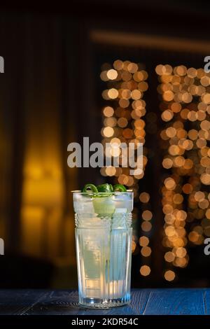 Cocktail with cucumber on a bar counter in a night club. Fresh cocktail on a bar with lighting bokeh background. Stock Photo