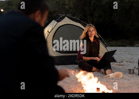 Young woman freelancer traveler working online using laptop and enjoying the beautiful nature landscape at sunset. Couple in love working relaxing in Stock Photo