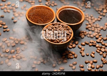 Set of three cups of coffee beans, ground and drink on black background, top view of coffee. Stock Photo