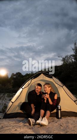 Young couple in love man and woman hug each other on the deserted beach on a summer evening at sunset during camping. banner. Stock Photo