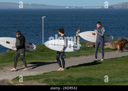 Three surfers carrying their surfboards and walking along the coast path at Newequay in Cornwall in England in the UK. Stock Photo