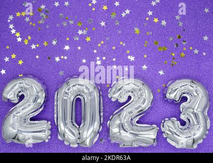 Inflatable shiny silver numbers of the New year 2023 on purple, very peri color background with shiny golden and silver stars. Copy space. Stock Photo