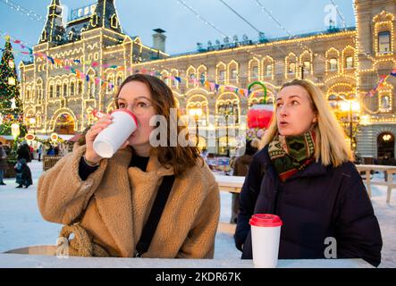 Two young women drink mulled wine with cardboard cups. Christmas fair on Red Square, Moscow. Stock Photo