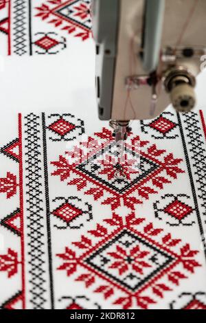Machine cross-stitch. Cross-stitch with red and black threads on canvas. Cross stitch on a sewing machine, close-up, selective focus. Ukrainian rushny Stock Photo