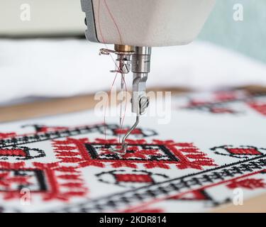 Machine cross-stitch. Cross-stitch with red and black threads on canvas. Cross stitch on a sewing machine, close-up, selective focus. Ukrainian rushny Stock Photo