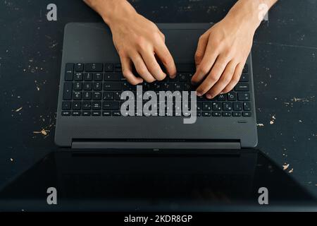 Close-up high angle view of unrecognizable business man typing texting on modern laptop keyboard, male employee sitting at black desk working on Stock Photo