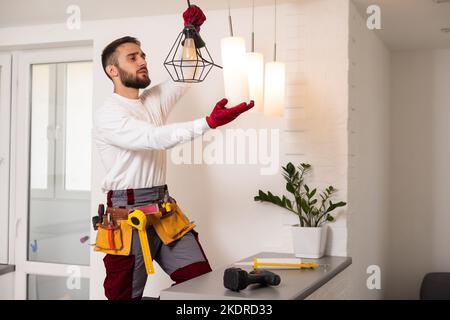 Electrician installs lamp lighting and spot loft style on ceiling. Stock Photo