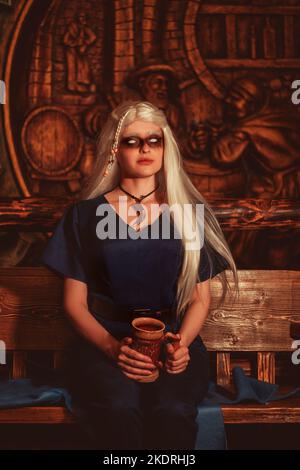 Viking woman with a mug in traditional warrior clothes inside a pub. Stock Photo