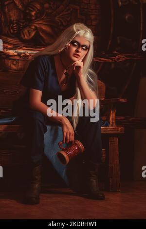 Viking woman with a mug in traditional warrior clothes inside a pub. Stock Photo