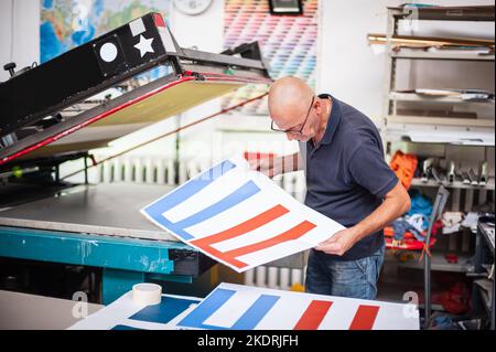 In the printing house, an experienced technician works on a screen printing machine. Production work. Check the print quality. Stock Photo