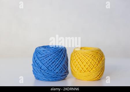 Close-up of two yellow and blue knitting balls side by side on a white table on a gray background Stock Photo
