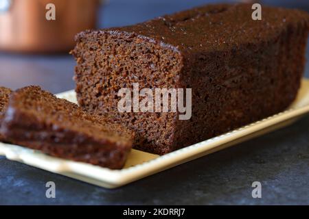 Jamaican ginger cake sliced homemade dark and spicy ginger and spice loaf cake on a vintage decorative cream oblong serving plate dark blue background Stock Photo