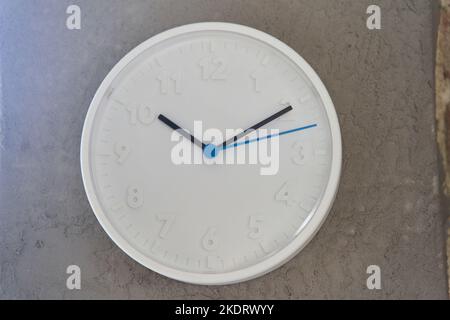 White big wall clock with blue second hand on rough cement wall Stock Photo