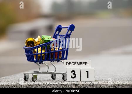 December 31 is written on a wooden plate in the calendar, and next to it is a cart from a supermarket with gifts on the street, happy new year, new ye Stock Photo