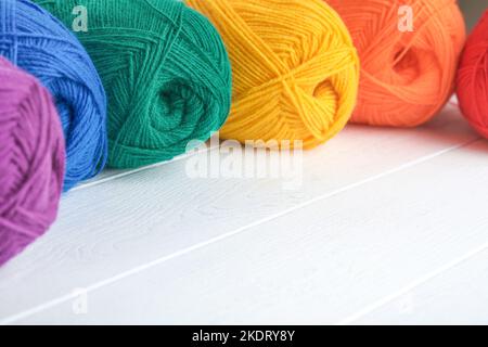 Many multi-colored balls of threads on knitted fabric on white wooden backgrounds. Yarn of bright colorful flowers, knitting and crocheting. Needlewor Stock Photo
