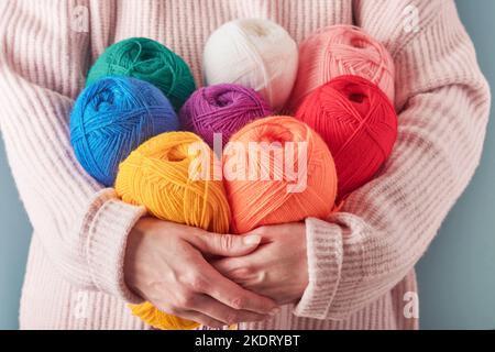 Female holding colorful or multicolored wool yarns on blue background. Many multi-colored balls of threads close-up. Needlework or knitting concept. Stock Photo