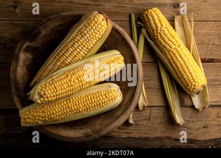 Aerial view of sweet corn cobs Zea mays in a wooden plate on a rustic table Stock Photo