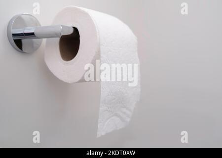 Single roll of toilet paper hangs on chrome holder. Narrow depth of field Stock Photo