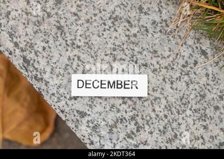 December is written on a wooden white board which lies on a stone road in the street, a calendar as a wallpaper Stock Photo