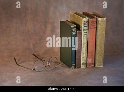 A stack of classic books waiting to be read, including Tarzan of the Apes, The Virginian, Modern Detective Stories, Rogue River Feud, The Wind In The Stock Photo