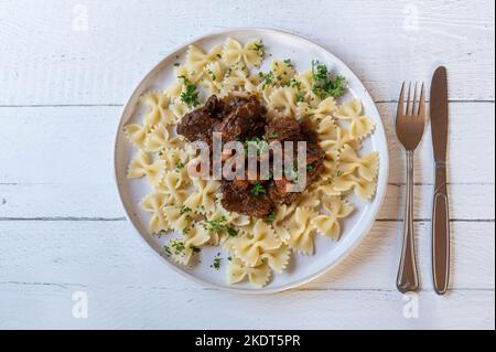 Brown beef stew with farfalle or bow tie pasta on a plate Stock Photo