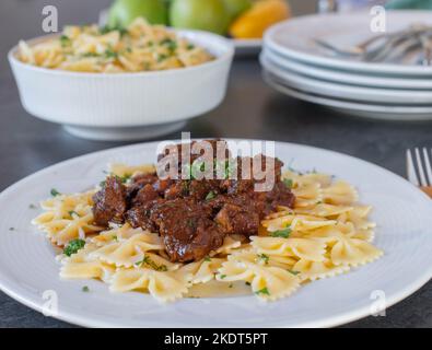 Beef goulash with farfalle pasta on a plate on kitchen table. Front view with blurred background Stock Photo