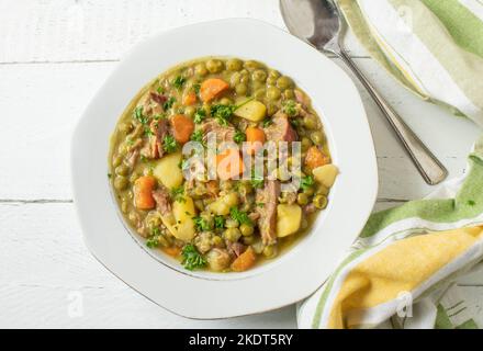 Pea stew on a white soup plate isolated on white wooden background from above Stock Photo