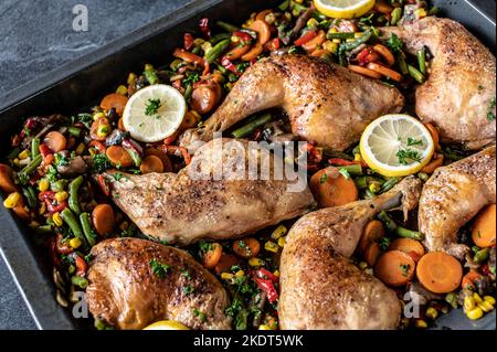 Roasted chicken legs with mixed vegetables on a baking tray	isolated on dark background from above Stock Photo