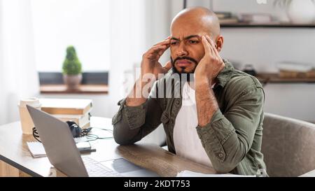 Freelance stress. Tired mature latin man looking at laptop screen and rubbing temples, sitting at desk at home Stock Photo
