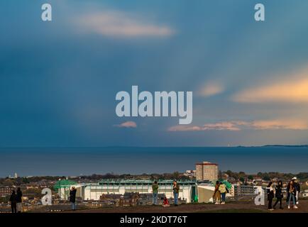 Calton Hill, Edinburgh, Scotland, UK, 8th November 2022. UK Weather: sunshine and cloud with tourists taking photos of the view across the Firth of Forth. The sky is split between dark cloud and sunlight with Hibernian Football Club stadium in the background. Credit: Sally Anderson/Alamy Live News Stock Photo