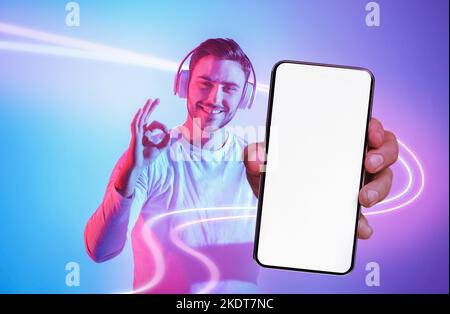 Handsome young man with headphones showing cell phone and okay Stock Photo