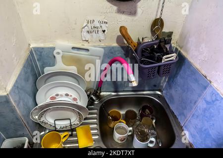 Dirty dishes unwashed in the sink with a sign "Keep clean lovely people". theme - shared kitchen, shared communal space. Stock Photo