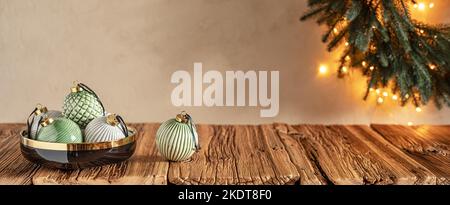 Pastel colored cozy Christmas background with baubles in black bowl on wooden table and wreath on wall Stock Photo