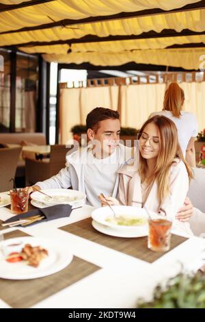 A cheerful and beautiful couple are relaxing on a summer terrace in a restaurant with food and drinks. The guy and the girl have fun on the terrace Stock Photo