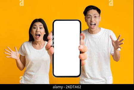 Amazing App. Surprised Young Asian Man And Woman Holding Big Blank Smartphone Stock Photo