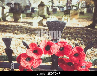 Red knitted poppies attached to the iron railings outside of the churchyard at St Mary's Church, Witney Oxfordshire for Remembrance Day. Stock Photo