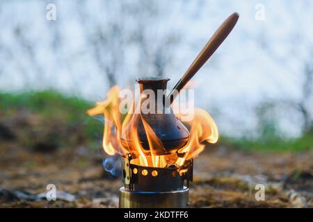 Making coffee process on campfire. Close-up coffee in turkish cezve on camping stove. Portable stove, which burned wood chips. Stock Photo