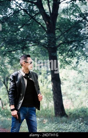 A man in dark glasses and a black leather jacket holds a gun in his hands Stock Photo