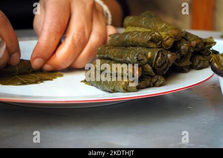 Grape Leaves Stuffed with rice and herbs .Woman preparing wrapped leaf. Stuffed grape leaves ready to cook. Turkish traditional food, Yaprak Sarma. Stock Photo