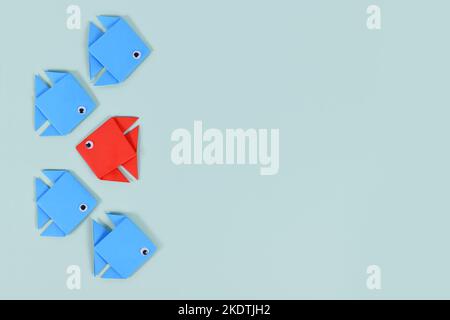 Red paper fish swimming swimming against the current in opposite direction of blue fish Stock Photo