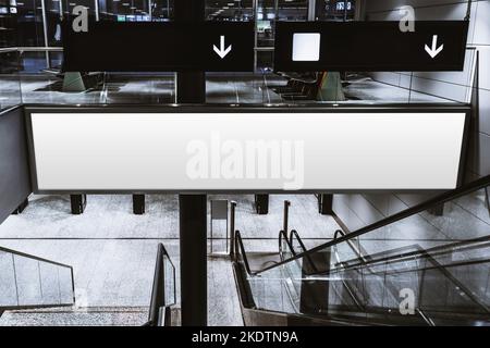 A mock-up placeholder of a blank indoor billboard over the stairs and an escalator in a modern airport terminal or a shopping mall; a template of a na Stock Photo
