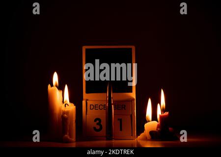 December 31 is written on wooden cubes and a combat bullet on a table in the dark, candles, Happy New Year, calendar and time of war in Ukraine Stock Photo