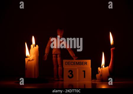 December 31 is written on wooden cubes, and next to it on the table in the dark is a wooden man and candles, Happy New Year, calendar Stock Photo