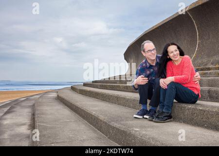 Couple seated on steps at beach Stock Photo