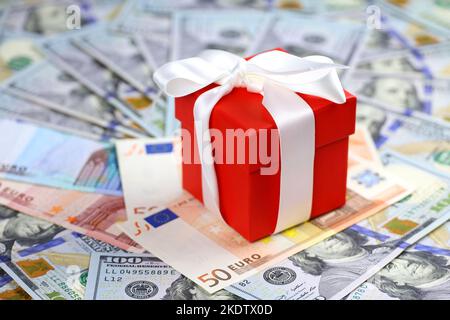 Red gift box wrapped with white ribbon on euro and US dollars background. Romantic surprise for Christmas holidays, New Year in United States and EU Stock Photo