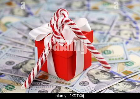 Red gift box and candy canes on US dollars background. Romantic surprise for Christmas holidays, buying souvenirs Stock Photo
