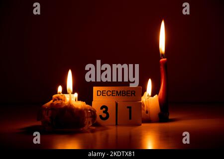 December 31 is written on wooden cubes that stand in the dark on the table next to candles at home, Happy New Year, calendar Stock Photo