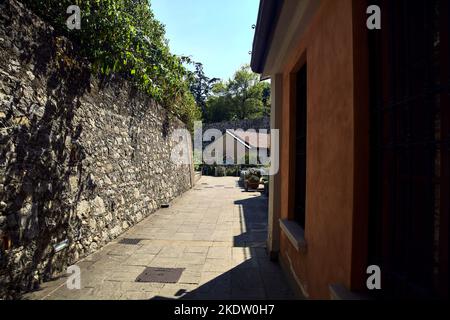 Paved path in a park between a stone wall and a building on a sunny day Stock Photo
